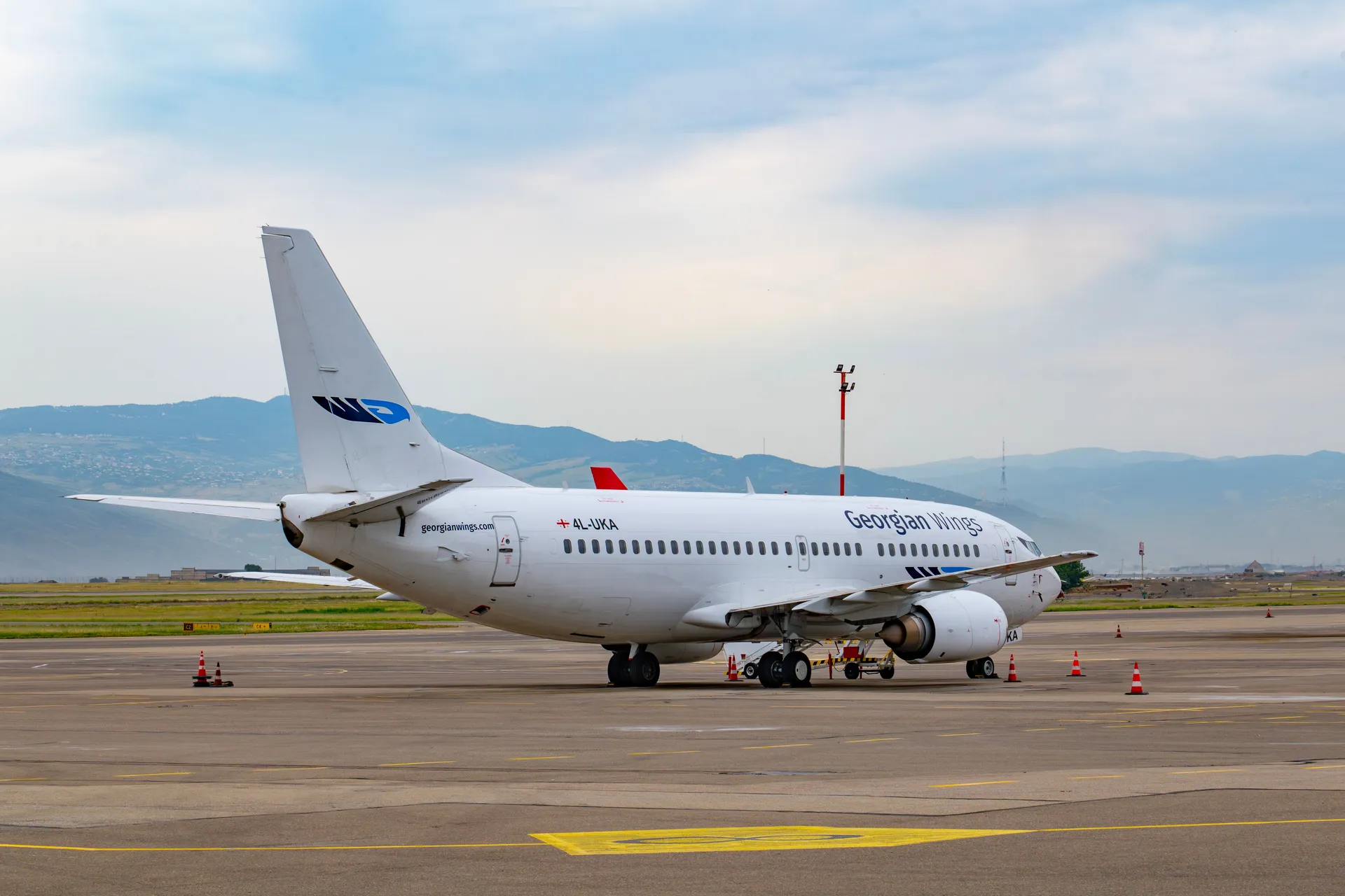 Georgian Wings aircraft parked at Tbilisi International Airport with mountains in the background